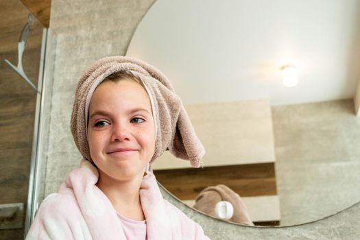 Relaxed young girl model wears towel wrapped on head, feels refreshed after taking shower, has healthy clean soft skin, poses in cozy bathroom. Girl, beauty and hygiene concept. High quality photo