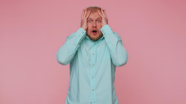 Stressed depressed adult man 30 years old in blue shirt expresses his fear and waves his hands away from danger, waving no. Scared fearful young guy isolated alone on pink studio wall background