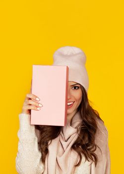 Happy young woman with a gift box in her hands, covers half of her face with a New Year's gift. The girl shows a gift to the camera. The concept of gifts and surprises for the new year and christmas.