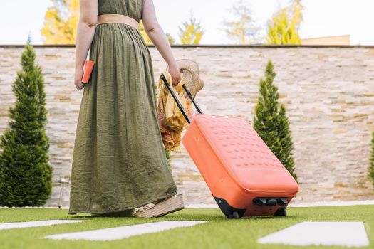 cropped shot of a young woman, entering hotel reception with her wheeled suitcase. woman on recreational trip. Outside, dim sunlight, grass floor with white tiles.