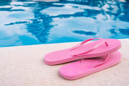 Close-up of pink flip flops for swimming pool or beach. Swimming pool water texture. Pool background with summer objects. Natural light outside. Sunny day.