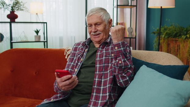 Overjoyed senior grandfather man hold smartphone look at screen excited about mobile app sport bet bid win. Happy elderly grandpa winner celebrate victory success read good news in cell text message