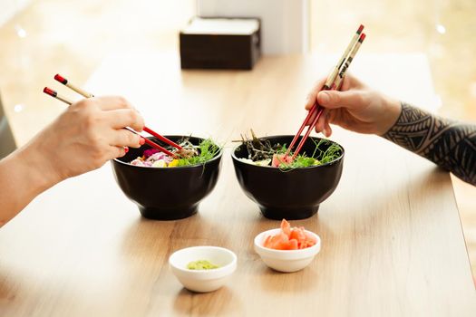 Man and woman eating poke salad with chopsticks. Dab tuna salad in a bowl. People in the restaurant eat salad with chopsticks. Asian seafood salad concept