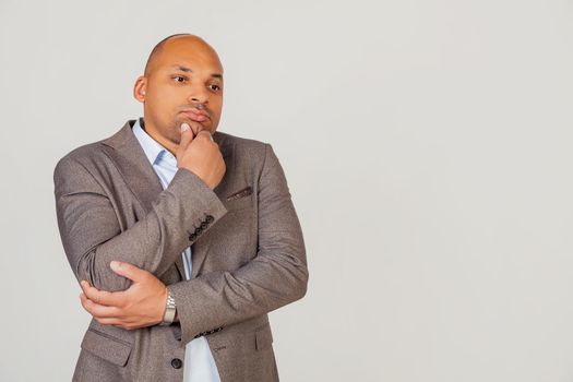 Handsome young male African American, businessman in jacket looking to the side and thinking touching chin with hand looking to the side with pensive facial expression.
