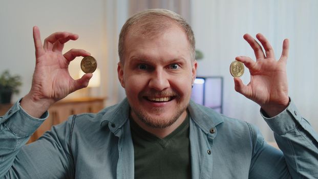 Man freelancer holding two gold coins at home, successful developer programmer. Guy stock trader earning bitcoins after online monitoring trading operations. Increasing wealth, financial prosperity