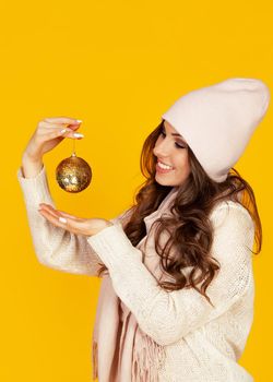 Happy young smiling woman holding a christmas tree ball promoting a best offer christmas tree. A girl in a sweater looks at a Christmas tree toy. New year and christmas holiday concept