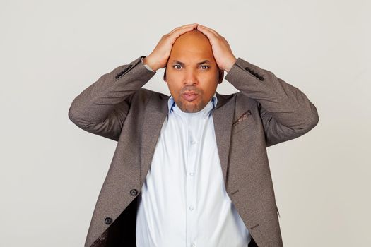 Upset shocked young African American guy businessman, holding hands on his head, was shocked by frowning and grabbing his head. Standing on a gray background