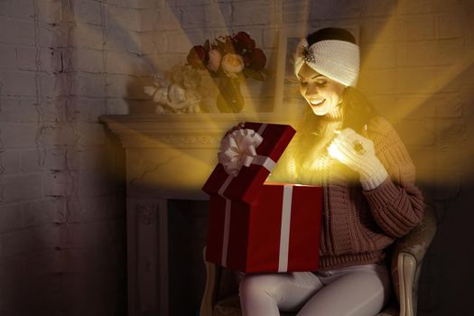 Happy young woman with a present, opening a Christmas present box. Portrait of happy smiling girl opening gift box isolated on red background