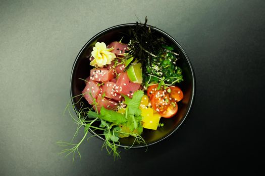 Poke salad with tuna in a bowl. Ingredients fresh tuna, cherry tomatoes, marinated seaweed, rice, takuan, Ponzu sauce, Teriyaki sauce, nori, sesame seeds, lime, cilantro. Asian seafood salad concept