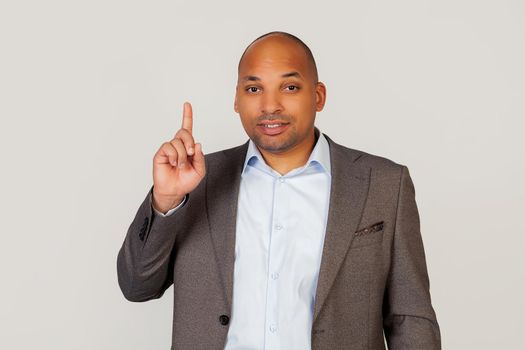 Happy young male African American businessman smiling with teeth and pointing thumb up with smiling face. Pointing hand and finger to the side, looking into the camera. Copy space for your ad.