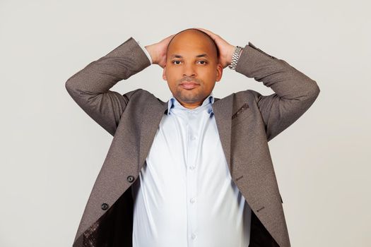 Portrait of a tired young African American guy businessman looking at the camera holding his hands behind his head, leaning back in a chair to rest a few minutes on a hard day in the office.