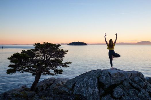 Young woman practicing yoga on a rocky island during a vibrant sunset. Taken in Whytecliff Park, Horseshoe Bay, West Vancouver, British Columbia, Canada.