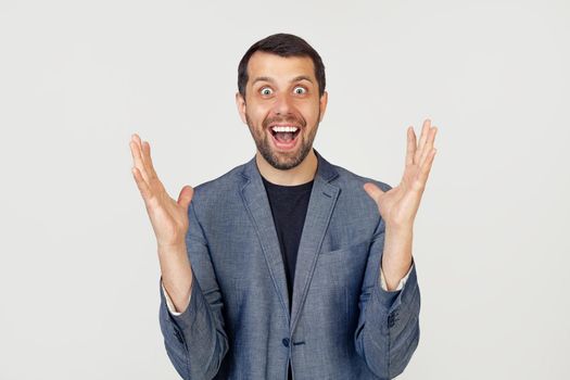 Young businessman with a smile man with a beard in a jacket, notes crazy and amazed with success with raised hands and open eyes shouting excitedly. Winner concept.