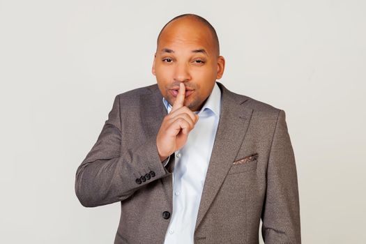 Man african american businessman in a jacket makes a gesture with his hand holding a finger on his lips, asks for silence and silence.