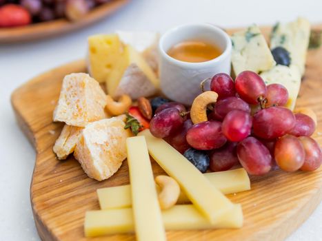 Wooden cutting board with refreshment - different kinds of cheese, grapes, honey and nuts.