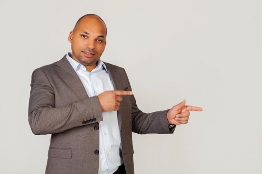 Happy young male African American businessman smiling happily and pointing to the side with index fingers on both hands while looking into the camera. Copy space for your ad