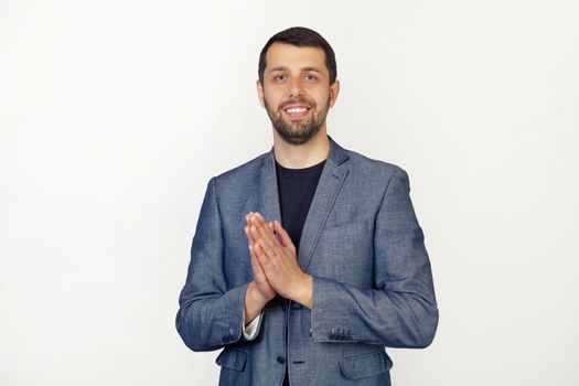 Young businessman man with beard Hands together and fingers crossed, smiling relaxed and cheerful. Success and optimism. Portrait of a man on a gray background.