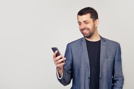 Portrait of a young male entrepreneur with a beard, modern, having a smartphone in his hands, busy checking e-mail, reading a message in the messenger, browsing or sending SMS using 5G, Wi-Fi