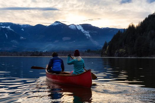 Adventurous people on a wooden canoe are enjoying the Canadian Mountain Landscape during a vibrant sunset. Taken in Harrison River, East of Vancouver, British Columbia, Canada.