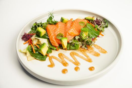 Salmon and avocado salad in tamarind sauce on a plate. Ingredients Iceberg lettuce, salmon, avocado, spinach, carrot, tamarind sauce. For restaurant menu.