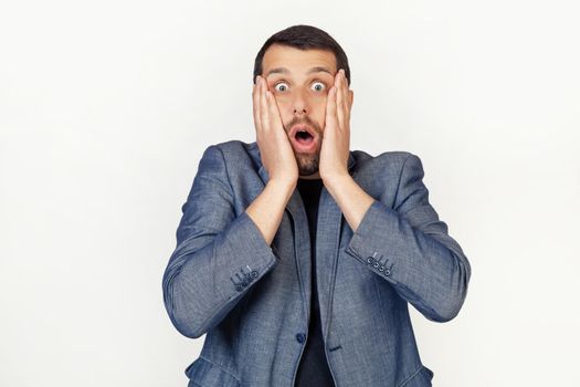 Young businessman man with a beard scared and shocked, surprised and surprised with hands on his face. Portrait of a man on a gray background.