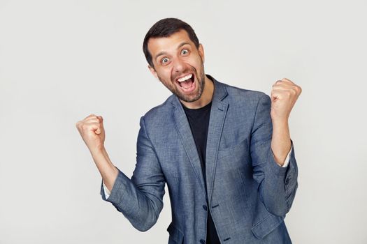 Young businessman with a smile man with a beard in a jacket, very happy and excited, making a winner gesture with raised hands, smiling and shouting about success. Celebration concept