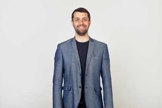 Young businessman with a smile, a man with a beard in a jacket, with a happy and cool smile on his face. Lucky person. Portrait of a man on a gray background.