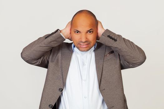 Upset man african american businessman in jacket, covering his ears with hands, hearing annoying sound, he has headache, posing for camera and covering his ears due to noise.