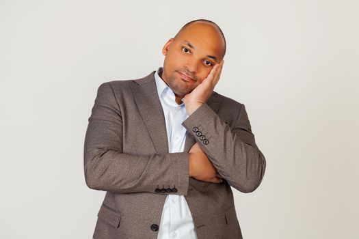 Portrait of a young african american guy businessman holding his hand on his face and staring indifferently at the camera, thinks he looks tired and depressed with crossed arms. gray background.