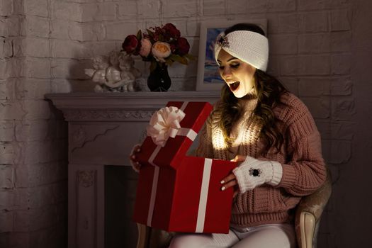 Happy young woman with a present, opening a Christmas present box. Portrait of happy smiling girl opening gift box isolated on red background