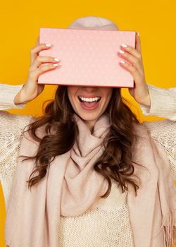 Happy young woman with a gift box in her hands, covers half of her face with a New Year's gift. The girl shows a gift to the camera. The concept of gifts and surprises for the new year and christmas.