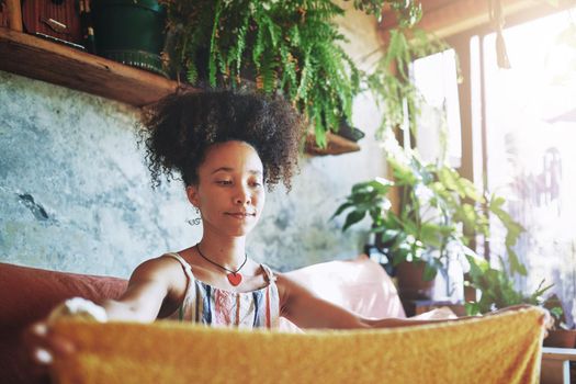 Shot of a beautiful African woman folding washed laundry while sitting on her couch - Stock Photo