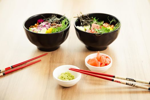 Two poke salads with beef and tuna in a bowl with various sauces on the restaurant table. Poke salads in a bowl next to chopsticks and ginger with wasabi. Asian salad concept.