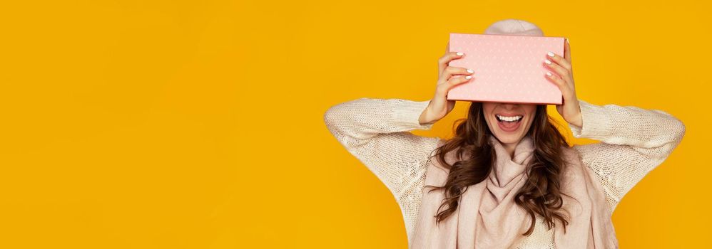 Happy young woman with a gift box in her hands, covers half of her face with a New Year's gift. The girl shows a gift to the camera. The concept of gifts and surprises for the new year and christmas.