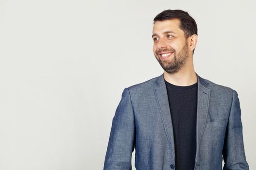 Closeup of a handsome bearded guy in a jacket standing in profile, looking to the side, posing for a photo. A man looking away to the side with a smile on the face, natural expression.