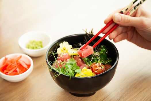A man eats a Poke salad with tuna in a bowl with chopsticks. Place the tuna salad in a bowl. Young man guy in a restaurant eating poke salad. Asian seafood salad concept