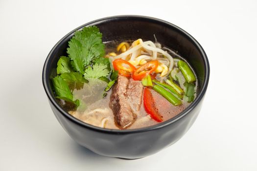 Asian soup with beef and Udon noodles in a black karelian. Ingredients broth, beef, bell pepper, Udon noodles, soy sprouts, miso paste, soy sauce, green onions, vegetable oil, chili peppers, garlic, cilantro. For restaurant menu.