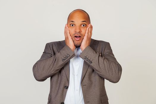 Shocked young african american guy businessman expressing surprise and amazement, touching his face and folding his lips, stands in a stupor and goggles at the camera, being impressed
