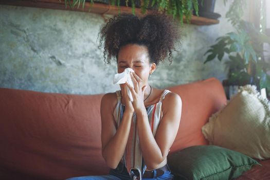 Shot of a young African woman blowing her nose in her living room