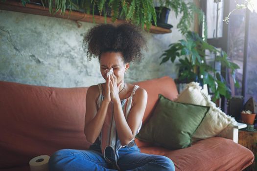 Shot of a young African woman blowing her nose in her living room