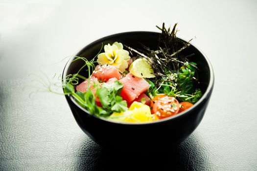 Poke salad with tuna in a bowl. Ingredients fresh tuna, cherry tomatoes, marinated seaweed, rice, takuan, Ponzu sauce, Teriyaki sauce, nori, sesame seeds, lime, cilantro. Asian seafood salad concept