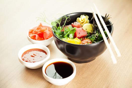 Poke salad with tuna in a bowl. Ingredients fresh tuna, cherry tomatoes, marinated seaweed, rice, takuan, Ponzu sauce, Teriyaki sauce, nori, sesame seeds, lime, cilantro. Asian seafood salad concept