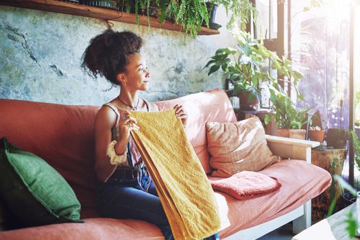 Shot of a beautiful African woman folding washed laundry while sitting on her couch - Stock Photo