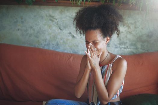 Shot of a young African woman blowing her nose in her living room