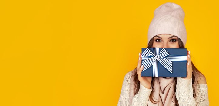 Happy young woman with a gift box in her hands, covers half of her face with a New Year's gift. The girl shows a gift to the camera. The concept of gifts and surprises for the new year and christmas.