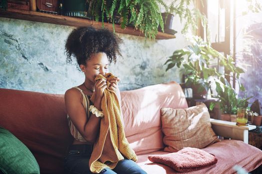 Shot of a beautiful African woman smelling freshly washed laundry while sitting on her couch - Stock Photo