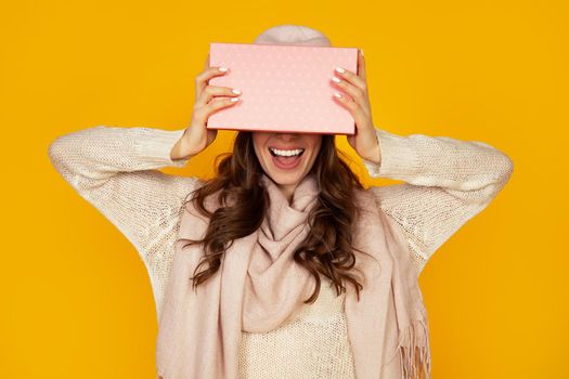 Happy young woman with a gift box in her hands, covers half of her face with a New Year's gift. The girl shows a gift to the camera. The concept of gifts and surprises for the new year and christmas.