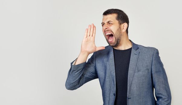 A young man with a beard screams out loud with his hand near his mouth. The concept of communication, news messages and attract attention.