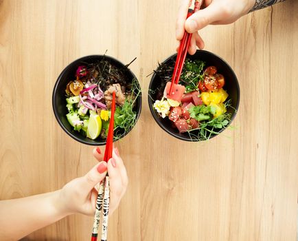 Man and woman eating poke salad with chopsticks. Dab tuna salad in a bowl. People in the restaurant eat salad with chopsticks. Asian seafood salad concept