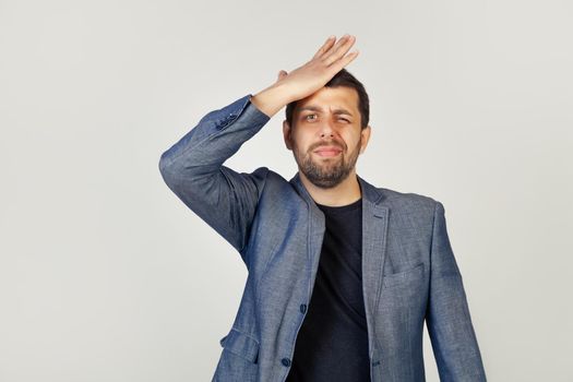 Young man businessman, resting his hand on his forehead, remembering something important, he forgets on a gray background. A man suddenly recalling big sales in stores